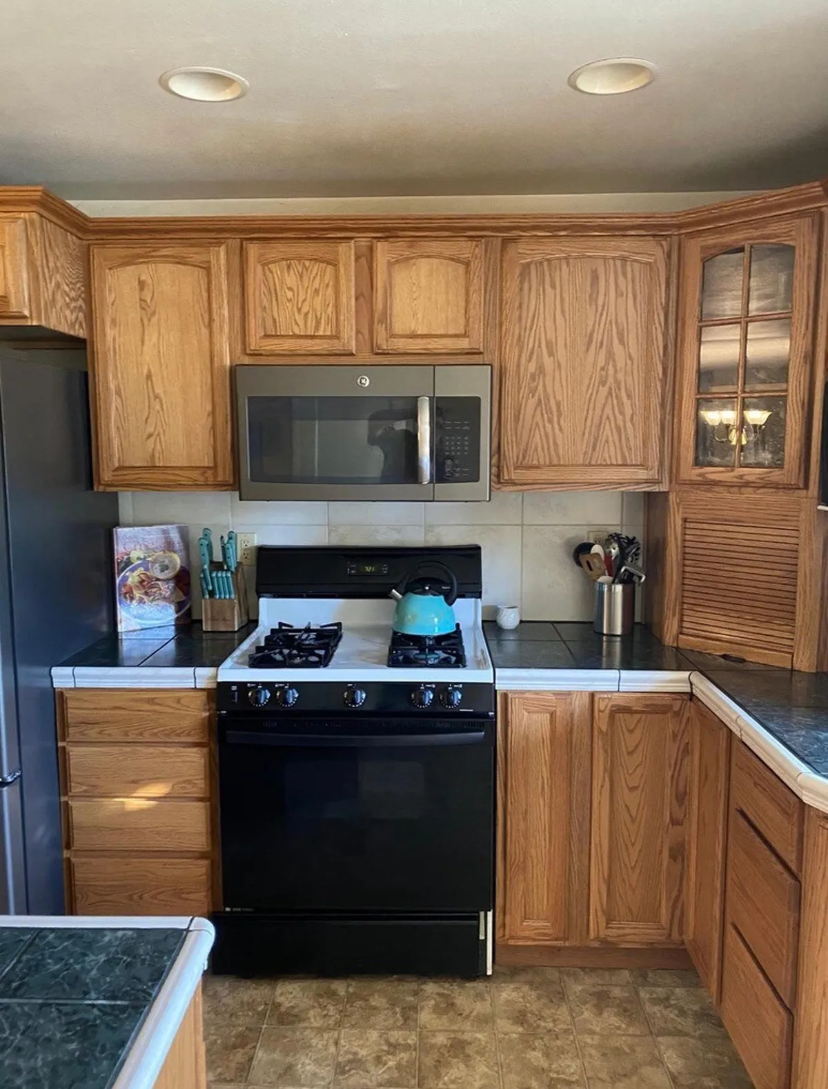 A cozy, open-concept kitchen with oak cabinetry, modern appliances, and a kettle set on the counter. The space is clearly designed for gatherings, meal prepping, and social interaction, with plenty of room for multiple people to cook or chat together.