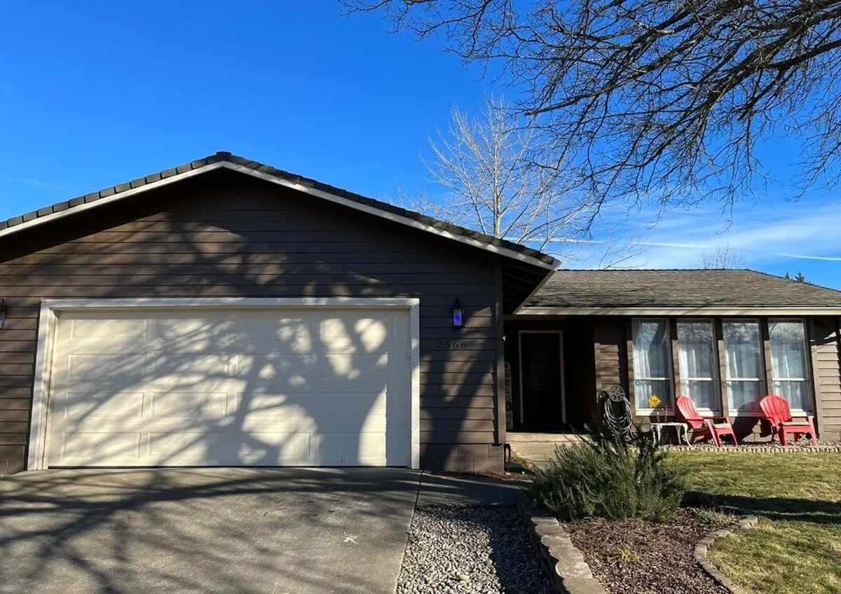 This exterior image features the home's garage door, a welcoming front porch with bright red chairs, and well-tended landscaping. The scene suggests an inviting entrance and a comfortable spot for families to relax outdoors together.
