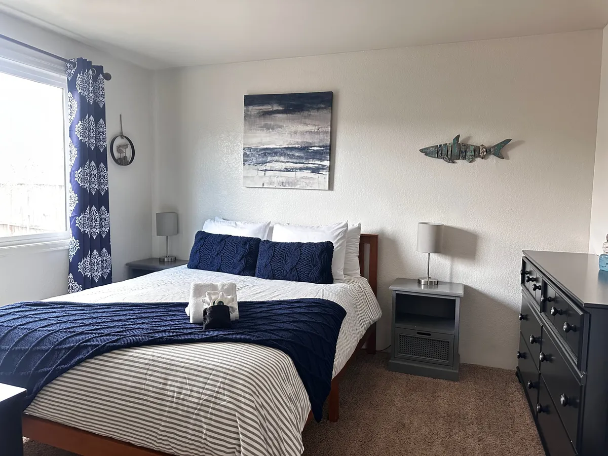 This scene features a king-sized bed adorned with a navy blue throw, large artwork above the headboard, decorative fish on the wall, a nightstand with a lamp, and soft natural lighting. The ambiance is serene and cozy, perfect for relaxation and rejuvenation.