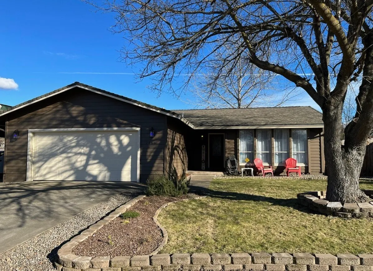 This exterior shot focuses on the main entrance of the home, featuring large windows and red Adirondack chairs on the porch. A large tree provides shade over the yard, and the setting exudes a cozy, inviting vibe. The space is perfect for unwinding or keeping an eye on kids playing nearby.