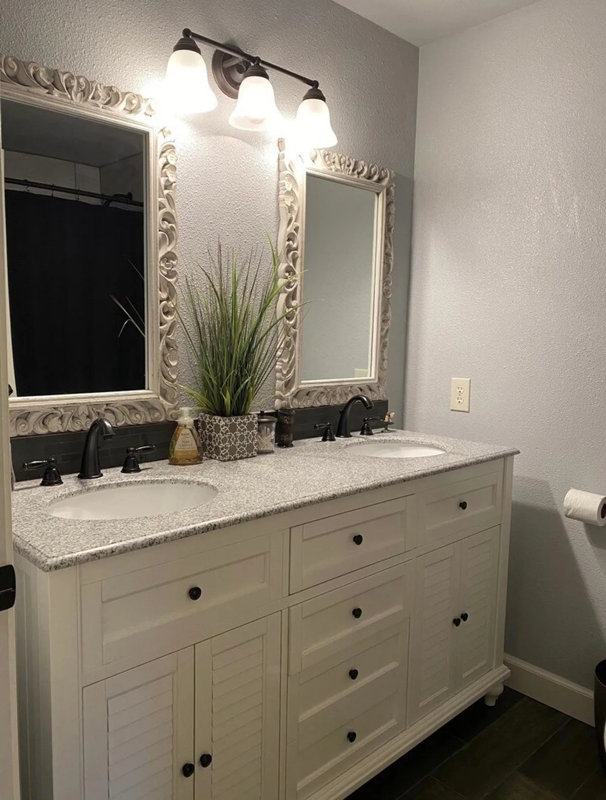 A double vanity sink with ornate mirrors and decorative plants, flanked by elegant lighting fixtures, creating a serene bathroom atmosphere. Morning light filters in, offering a shared yet private space for self-care routines.