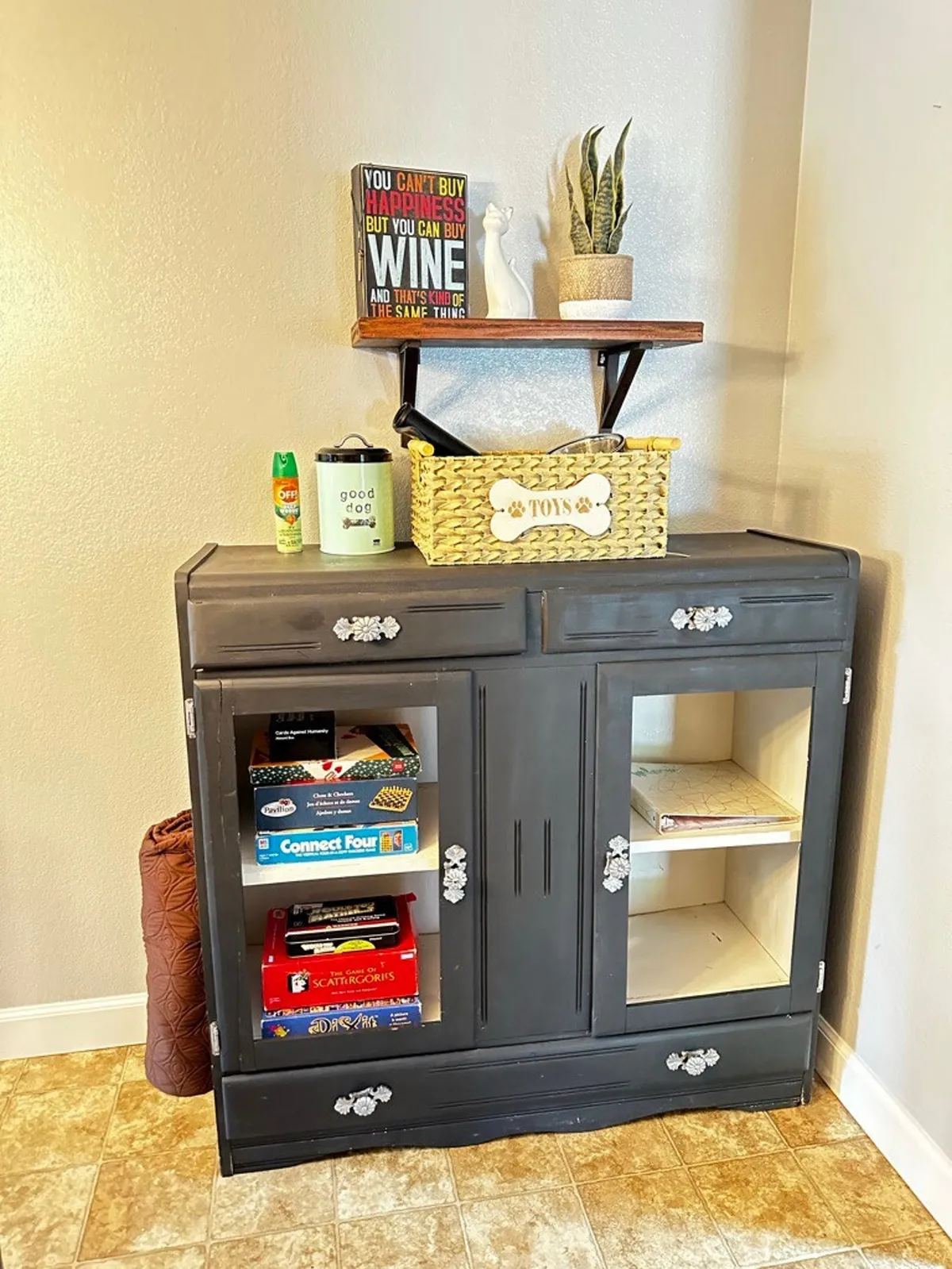 This playful and cozy room features a cabinet topped by a decorative sign, a potted houseplant, and a basket of toys—suggesting a space where game nights, playful interactions, and relaxed evenings take place. The ambiance is casual and family-friendly.