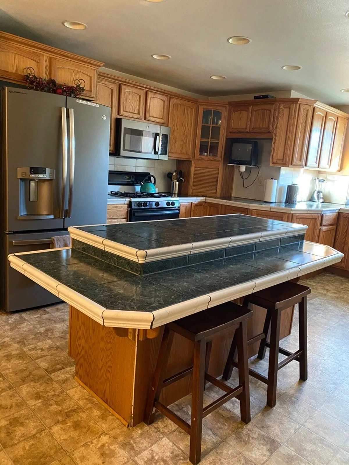 A spacious, fully equipped kitchen with a central island featuring a green countertop, stove, refrigerator, and wooden cabinets—set up for group cooking and family get-togethers.