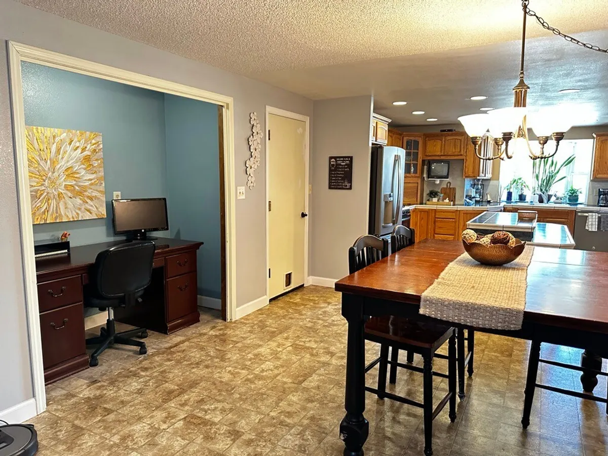 A wide-angle view connects the dining table, kitchen island, and a workspace. The scene is set for family meals, home office work, and social gatherings, embodying the flexibility of modern communal spaces.