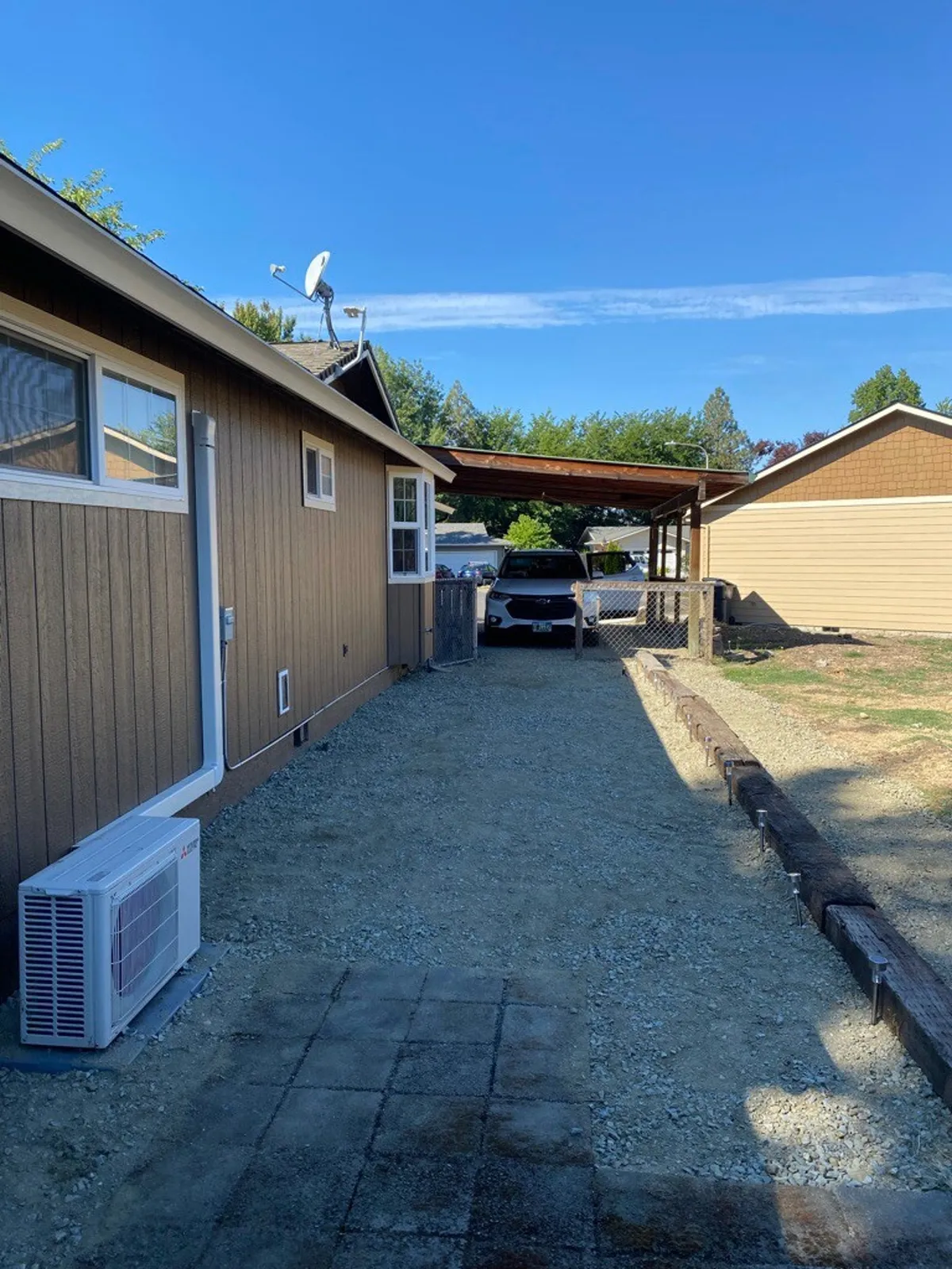 This image presents the house’s exterior with a view of the carport, surrounding landscape, and open sky. The yard offers plenty of room for gatherings, and the open atmosphere hints at possibilities for stargazing or hosting social events in the evening.